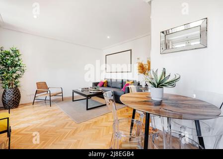 tavolo da pranzo rotondo in legno con sedie in metacrilato trasparente in un soggiorno con divano letto e tavolini laterali bassi Foto Stock