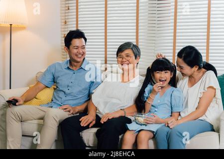 Famiglia asiatica multi generazionale di padre, madre, figlia e nonna che guarda la TV sul divano nel soggiorno Foto Stock