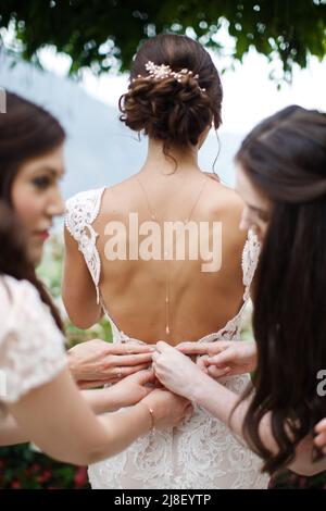 Bridesmaids aiutare la sposa mettere sul suo vestito. Foto Stock