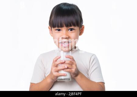 Asian piccola ragazza carina bere latte da un bicchiere su sfondo bianco in studio. Nutrizione sana per i bambini piccoli. Foto Stock