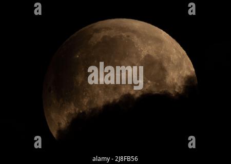 Londra, Regno Unito. 16th maggio 2022. UK Weather: Super Blood Moon - Eclipse parziale alle 03:24. Una spettacolare luna di sangue super è visto entrare nelle prime fasi di un'eclissi lunare totale con una debole ombra che inizia a scurire dall'alto a sinistra come visto dal sud-est di Londra appena prima della copertura della nuvola. La luna appare rossa quando cade nell’ombra della Terra. L’effetto è causato dall’atmosfera terrestre che piega verso di essa parte della luce solare. L’unica eclissi lunare piena di quest’anno si sta verificando durante una super luna, quando la luna si trova nel punto più vicino alla Terra nella sua orbita, facendola apparire più grande. Credito: Foto Stock