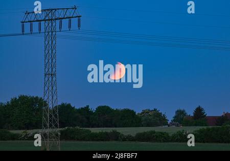 Jacobsdorf, Germania. 16th maggio 2022. L'inizio di un'eclissi lunare può essere visto al mattino presto sopra il paesaggio accanto ad un pilone ad alta tensione. Credit: Patrick Pleul/dpa/Alamy Live News Foto Stock