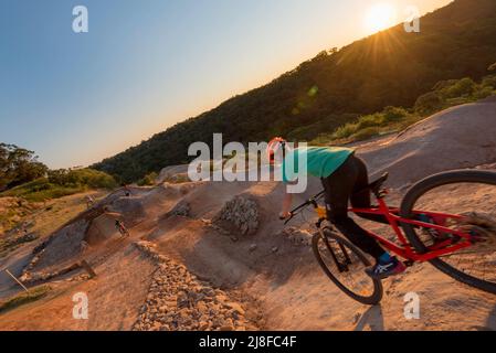 Un giovane motociclista in mountain bike che passa sopra la cresta di una ripida discesa, collina al parco ciclistico Jubilee Oval a Wahroonga, Sydney, nuovo Galles del Sud, Australia Foto Stock