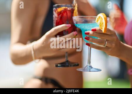 Due mani femminili abbronzate con bicchieri di cocktail freschi, decorate con una fetta di arancio. Vista del raccolto delle mani della donna con manicure che tiene le bevande per brindisi in vacanza. Concetto di celebrazione. Foto Stock