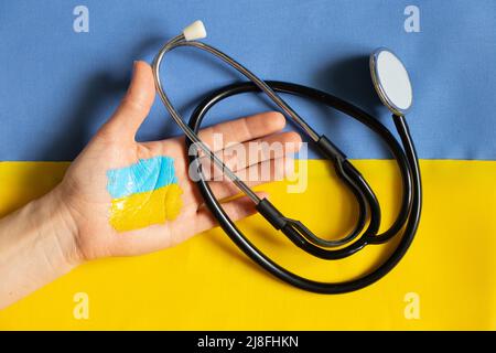 Stetoscopio in mano si trova sulla bandiera nazionale dell'Ucraina giallo-blu, legge marziale in Ucraina, assistenza medica in guerra Foto Stock