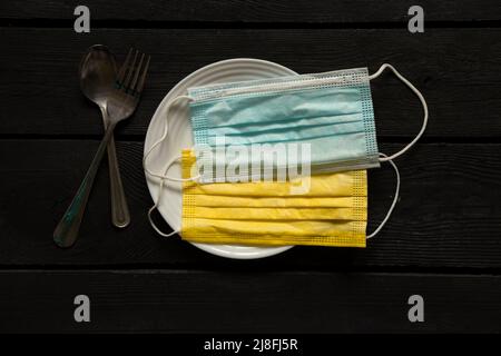 Maschere mediche giallo-blu come la bandiera dell'Ucraina si trova su un piatto su un tavolo di legno nero. Bandiera nazionale dell'Ucraina, fermare la guerra. La Russia è l'aggr Foto Stock