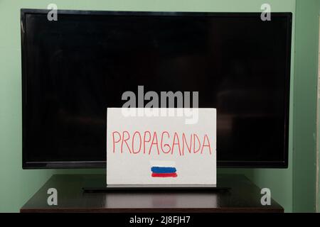 La parola propaganda e la bandiera della Russia è scritta su un piatto che pende sulla TV, propaganda russa attenzione, fermare la guerra in Ucraina Foto Stock
