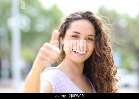 Fronte vie writratto di una donna felice gesturing thumbs in su sorridendo in un parco Foto Stock