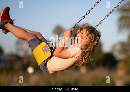 Ritratto emozionale di un bambino nel parco giochi. Attività all'aperto per bambini. Ragazzino che si diverte a fare un'altalena sul parco giochi nel parco pubblico in autunno Foto Stock