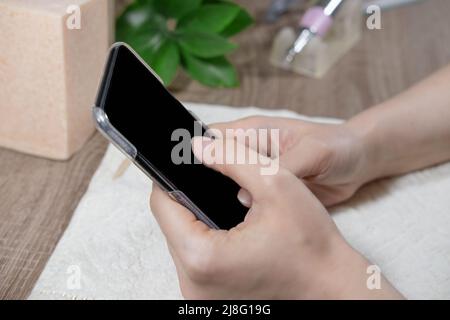 Mani femminili con uno smartphone su sfondo bianco con piante. Dispositivi digitali. Social network, comunicazione online, shopping, lifestyle. Online Foto Stock