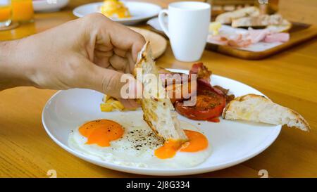 Uomo a mano immergere il pane tostato in tuorlo d'uovo fritto nel ristorante a colazione o pranzo Foto Stock