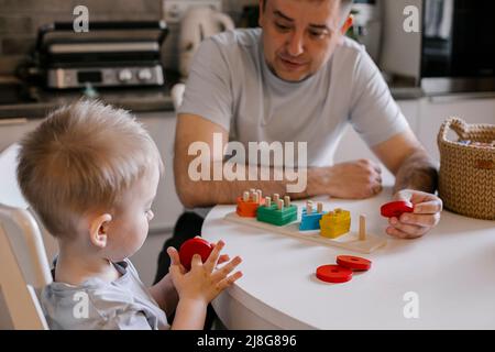 Il padre e il figlio del bambino giocano insieme. Piccolo ragazzo carino con papà raccogliere il selezionatore colorato. Stile di vita familiare, sviluppo precoce dei bambini, istruzione Foto Stock