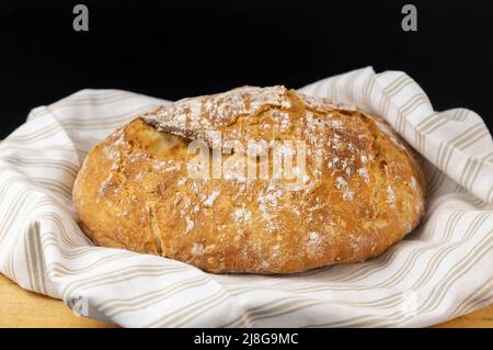 Pane fatto in casa. Pane rotondo appena sfornato su un fondo di legno, messo su un asciugamano di colore chiaro. Foto Stock
