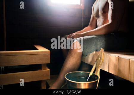 Sauna in Finlandia. Uomo che si rilassa in bagno turco nel centro benessere, cabina, casa o hotel benessere. Tradizionale estate finlandese. Interni in legno vecchio. Secchio dell'acqua. Foto Stock