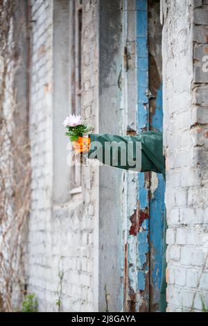 Un uomo in un impermeabile e maschera a gas raccoglie un fiore da una terra bruciata e velenosa. Concetto di inquinamento atmosferico. Catastrofia ecologica. Foto Stock