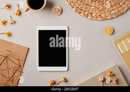 Tavoletta digitale circondata da fiori decorativi secchi, tazza di caffè, carta, vaso o candelabro fatto a mano, copybook e taccuino Foto Stock
