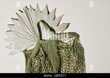 Flatlay di borsa in maglia verde fatta a mano con ventilatore di colore grigio pastello all'interno su sfondo bianco con copyspace per il tuo testo a destra Foto Stock