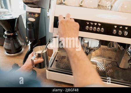 Primo piano delle mani del barista che scalda il latte nella caraffa con il vapore Foto Stock
