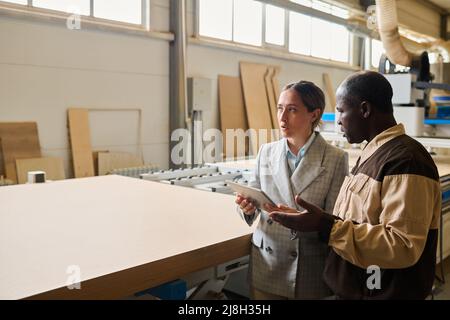 Ingegnere femminile che utilizza un tablet pc e discute del lavoro della macchina con il caposquadra in fabbrica Foto Stock