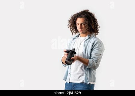 Il giovane uomo con capelli ricci sta tenendo una macchina fotografica sulla sua mano. Concetto di hobby e fotografia. Foto di alta qualità Foto Stock