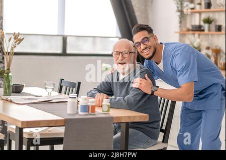 Pensionato e il suo caregiver in posa per la macchina fotografica in cucina Foto Stock