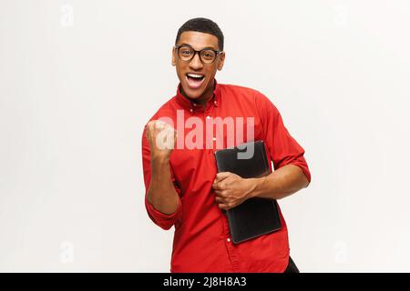 Eccitato overjoyed africano-americano giovane uomo in rosso casual shirt celebrare le buone notizie o vincere, esprime la felicità, ragazzo latino con laptop urlando sì in segno di trionfo Foto Stock