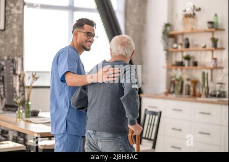 Infermiera che aiuta il paziente a camminare con un bastone Foto Stock