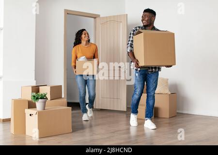 Joyful sposi neri che tiene le scatole di cartone che entrano nella nuova casa Foto Stock