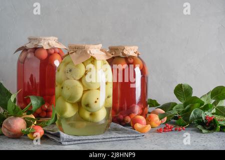 Tre conserve di frutta fatte in casa composta di mele e ciliegie in grandi vasi di vetro su tavola grigia. Foto Stock