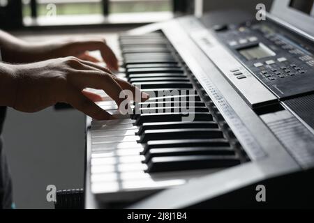 ragazzo latino che impara a suonare il pianoforte a casa. dettaglio delle mani di un uomo che suona una canzone sul suo sintetizzatore. luce naturale che passa attraverso la finestra. Foto Stock