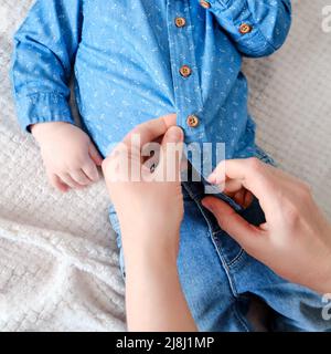 Una donna madre indossa una camicia blu a un bambino. La mamma indossa un bambino in abiti sul letto. Foto Stock