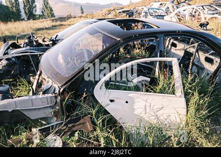 Discarica di auto, rottami di metallo. Primo piano di una vecchia auto abbandonata in un cortile con erba che germogliano all'interno e cobbweys troppo coltivati. Il sole si riflette Foto Stock