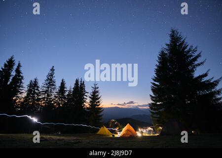 Luminose tende turistiche illuminate che brillano sul campeggio in montagne scure sotto il cielo notturno con stelle scintillanti. Concetto di stile di vita attivo Foto Stock