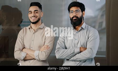 Due colleghi maschi felici multirazziale diversi uomini d'affari partner uomini ispanico uomo arabo barbuto ragazzo sorridendo in carica con le braccia incrociate Foto Stock