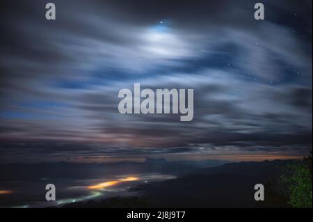 Paesaggio di nuvoloso soffiato attraverso il cielo blu con stelle e chiaro di luna sulla cima della montagna nel parco nazionale di notte. Lunga esposizione e movimento Foto Stock