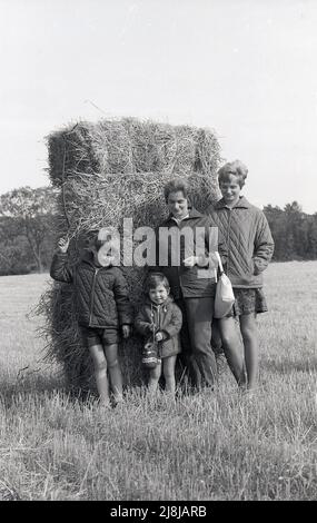 1970s, storiche, madri tw con i loro figli in un campo in piedi contro un fiocco rettangolare per la loro foto, tutti indossando le giacche leggere trapuntate, un capo di abbigliamento che era popolare in questa epoca, Inghilterra, Regno Unito. Foto Stock