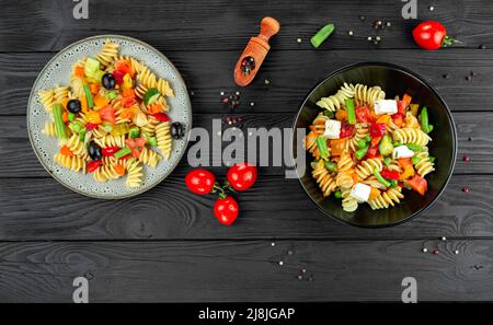 Penne pasta con verdure, piselli, peperoni dolci, pomodori, salsa, mozzarella su sfondo di legno nero. Pasta italiana con verdure e sp Foto Stock