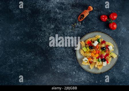 Penne pasta con verdure, piselli, peperoni dolci, pomodori, salsa, mozzarella su sfondo nero. Pasta italiana con verdure e spezie Foto Stock