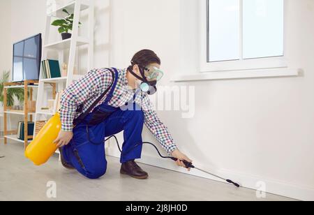 Il lavoratore di controllo di peste in una maschera e tute spruzzando insetticida all'interno della casa Foto Stock