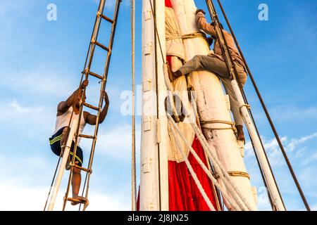 due uomini in alto sul palo che fissa il rigigng e vele Foto Stock