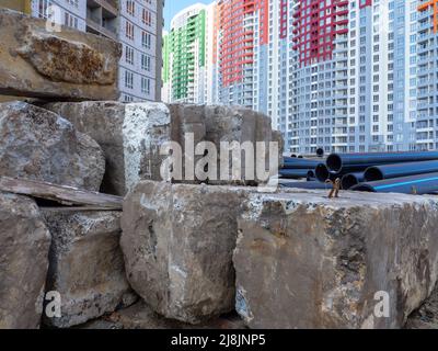 Un cantiere con enormi blocchi di cemento e grandi tubi neri in primo piano e nuovi e colorati edifici alti sullo sfondo a Kyiv, Ucraina. Foto Stock