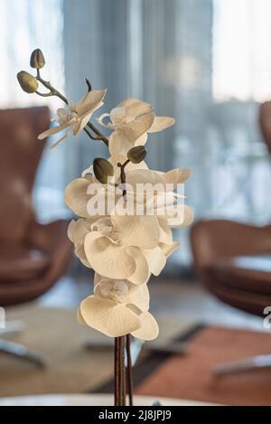 Primo piano di un'orchidea bianca artificiale con sfondo sfocato e sedie moderne in un luminoso ambiente aziendale, USA. Foto Stock