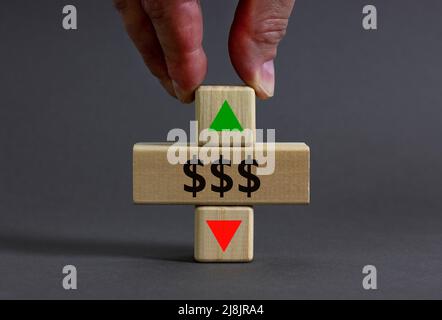 Simbolo dei tassi in dollari. L'uomo d'affari tiene un cubo di legno con la freccia che simboleggia che i tassi del dollaro stanno andando giù o su. Bello grigio tavolo grigio backgrou Foto Stock