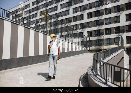 Il giovane corriere africano cammina lungo una strada cittadina con uno zaino termale, consegnando l'ordine da un ristorante o negozio. Il corriere parla al telefono e prende ordine. Consegna rapida di varie merci. Foto Stock