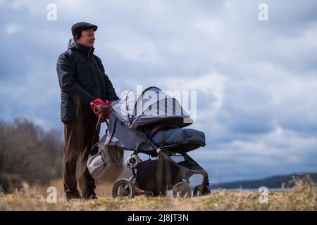 Nonno che cammina con un passeggino in primavera sulla natura Foto Stock