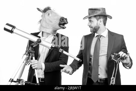 Uomo d'affari in testa a cavallo maschera tenere telescopio e uomo cowboy con binocolo, visione d'affari Foto Stock