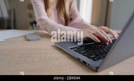 Mani femminili ravvicinate con documenti che ordinano i documenti digitando sul portatile al tavolo in ufficio. Lavoro di ufficio di donna di affari caucasica non riconoscibile a. Foto Stock