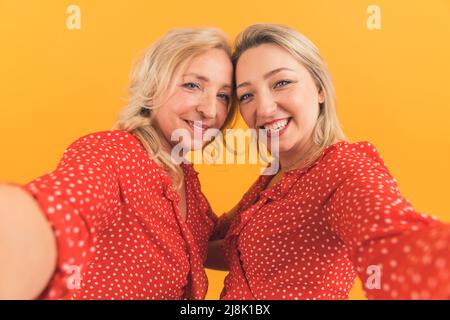 mamma e figlia che fanno insieme carino selfie su sfondo arancione, studio isolato. Foto di alta qualità Foto Stock