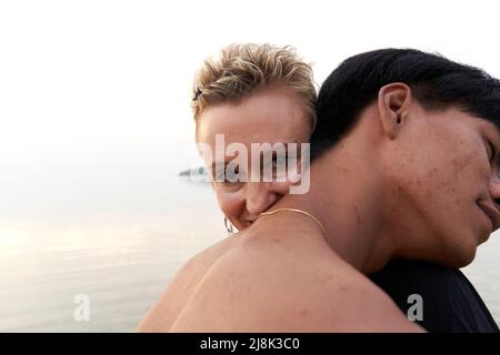Donna caucasica sorridente mentre abbraccia un giovane uomo asiatico vicino al mare Foto Stock