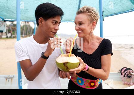 Coppia che si guardano l'un l'altro mentre condividono una noce di cocco naturale per bere in una spiaggia Foto Stock